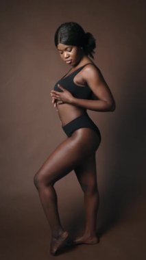 İç çamaşırlı, genç ve çekici bir Afro-Amerikan modelin vücuduna nazikçe dokunup kameraya baktığı dikey bir çekim.