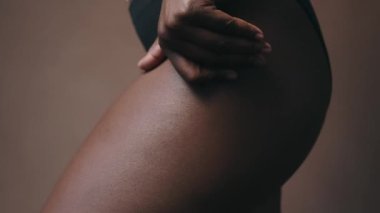 Stüdyoda dururken rahat iç çamaşırlarıyla vücudunu nazikçe okşayan, tanınamayan siyah kadın modelin yakın çekimi. Öz-sevgi, beden pozitifliği kavramları