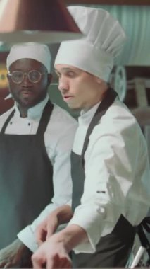 Kafkasyalı baş aşçının, lokanta mutfağında birlikte çalışırken siyah çırak için sipariş bileti eklerken dikey pozu.