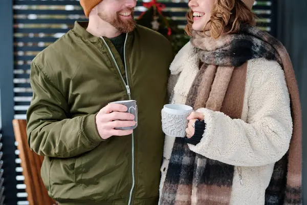 身穿保暖衣服 手持杯子站在室外的快乐白种人夫妇拍摄的中等产量照片 免版税图库照片