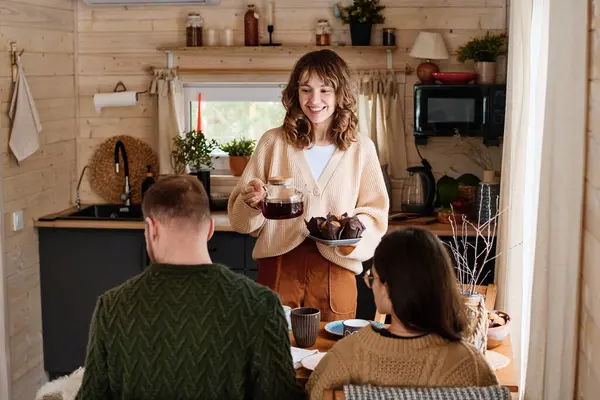 快乐的白人妇女与丈夫和女儿一起在乡村木屋里喝茶和吃松饼 图库图片