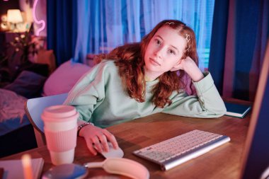 Modern beyaz kız portresi. Kızıl saçlı. Masasında oturmuş kameraya bakıyor.