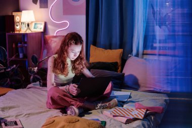 Modern Kafkasyalı genç kız akşamları yatak odasında oturur dizüstü bilgisayar ve fotokopi çekerek okul projesi üzerinde çalışır.