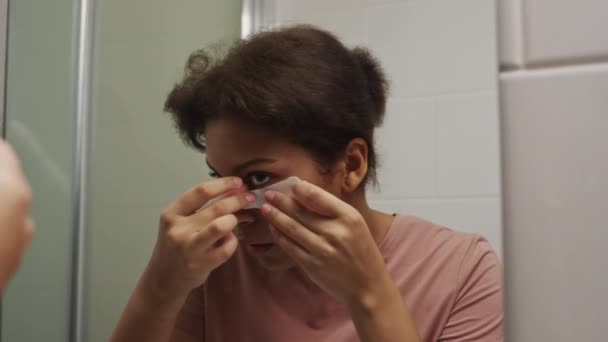 年轻的昏昏欲睡的女孩在浴室镜子前贴上眼罩 以消除家里早上的黑眼圈和浮肿 — 图库视频影像