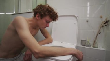 Genç akşamdan kalma adam sabahları evde partiden sonra midesi bulanırken banyoda tuvalete yaslanıyor.