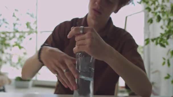Ung Man Svepa Tinsel Från Bordet Dricka Vatten Från Flaska — Stockvideo
