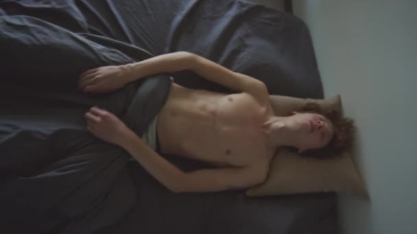 若いシャツレスの男がベッドに落ちて寝て パーティー後の朝に二日酔いに苦しんでいる最上階の景色 — ストック動画