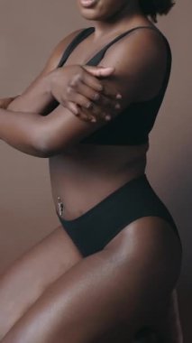 İç çamaşırlı, genç ve güzel bir Afro-Amerikan modelin dikey çekimi. Güzel bir vücuda özenle dokunuyor ve stüdyoda kameraya poz veriyor.