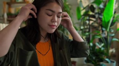 Ahşap koltukta oturan ve arka planda taşınabilir kasetçalar, çevre dostu yaprak döşeme aracılığı ile müzik dinleyen günlük kıyafetli beyaz bir kadın.