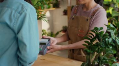 Bahçıvanlık mağazasında çalışan önlük giymiş, gülen İspanyol bir kadın. Arka planda çevre dostu bir ortam var.