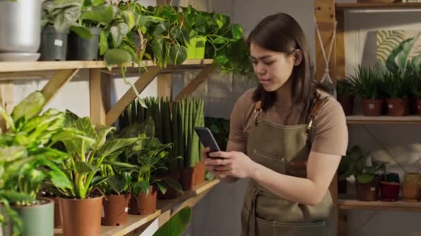 在绿色商店工作的中年白人妇女 拍摄可供送货或取货的家庭植物的照片 在社交媒体上做广告 — 图库视频影像