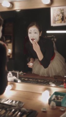 Pandomimci kadının makyaj yaptığı ve soyunma odasındaki aydınlatılmış aynaya bakıp tiyatroda sahne aldığı dikey bir sahne.