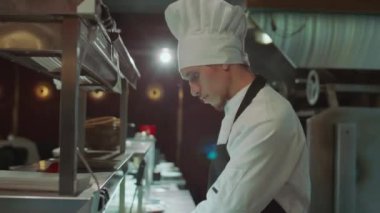 Önlüklü ve eldivenli yetenekli bir aşçı açık restoran mutfağında yemek siparişi verirken tabakta sebze servis ediyor.