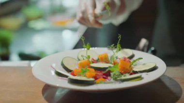 Eldivenli şefin tabakta servis edilen tabağa cımbızla taze ot ekleyip sonra da restoranın mutfağında garsonun siparişini aldığı yakın çekim.