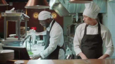 Neşeli Kafkas şefi yemek pişiriyor, Afrikalı Amerikalı iş arkadaşıyla konuşuyor ve restoran mutfağında çalışırken ona yumruk çakıyor.