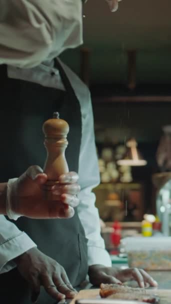 在餐馆厨房上菜前 厨师在围裙和手套中加入盐并使用胡椒磨来调味肉蒸的垂直镜头 — 图库视频影像