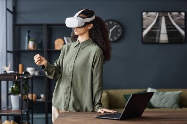 VR kulaklık takan genç bir kadın evdeki oturma odasında oturmuş internette sörf yapıyor, mekanı kopyalıyor.