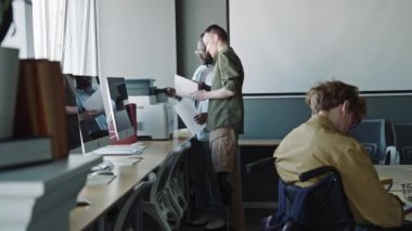 Beyaz, protez bacaklı genç bir adam ofiste siyahi bir erkek arkadaşla çalışırken belgelerin fotokopisini çekmek için yazıcı kullanıyor.