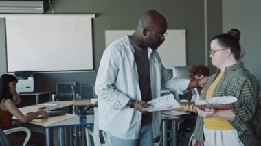 Afrika kökenli Amerikalı yönetici, Down sendromlu genç bayan stajyeri selamlıyor, belgelerini gösteriyor ve iş günlerinde iş görevlerini anlatıyor.