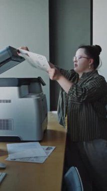 Down sendromlu genç bayan ofis müdürünün yazıcıdaki iş belgelerini kopyaladığı dikey çekim.