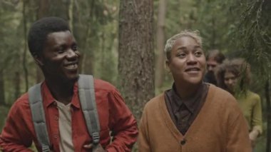 Çeşitli arkadaşlar hafta sonları doğa yürüyüşü yaparken ormanda birlikte yürüyor, gülümsüyor ve sohbet ediyorlar.