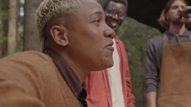 Arkadaşları yanında durup bira içerken ve kamp alanında gülümserken genç bir adamın gitar çalıp şarkı söylediği bir sahne.