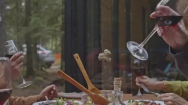 Bir grup arkadaşın şarap bardaklarıyla kadeh tokuştururken dışarıda, ormanda bir kulübede yemek masasında otururken yakın plan çekimleri.