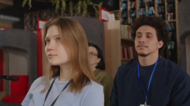 Üniversite kütüphanesindeki konferansı dinlerken genç öğrenciler izleyiciler arasında fısıldaşıyor ve gülümsüyor.