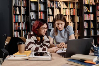 Üniversite kütüphanesinde engelli Asyalı genç kızla birlikte çalışan beyaz bir öğretmen, okul sınavlarına hazırlanıyor.