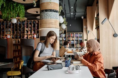 Üniversite kütüphanesinde birbirlerinin önünde oturan farklı etnik kız öğrenciler sınava ya da sınava hazırlanıyorlar.