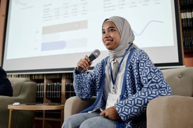 Düşük açılı orta açılı Müslüman kız tesettüre oturmuş üniversitedeki konferans sırasında mikrofonla konuşuyor.