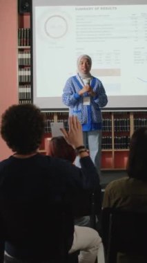 Eğitimsel konferans sırasında sunum yaparken tesettürlü Müslüman bir kızın mikrofonla konuşmasının dikey çekimi