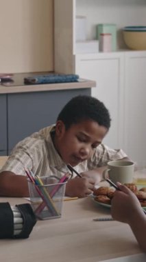 Orta boy Afro-Amerikan çocuğun kurabiye ile çay içtikten sonra mutfak masasında oturduğu dikey bir fotoğraf.