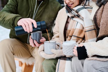 Tanımlanamayan bir adamın soğuk kış gününde ailesiyle bankta oturup sıcak çayı bardaklara dökerken görüntüsü.