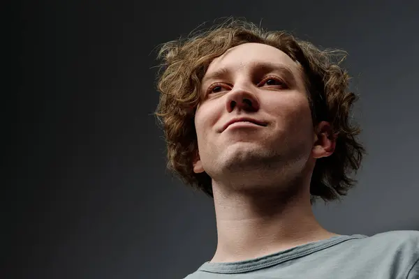 stock image Low angle closeup studio portrait of self-confident young Caucasian man with curly hair smirking, copy space