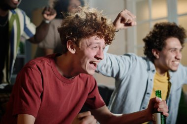 Neşeli, beyaz bir adam ve çok ırklı arkadaşlarının TV 'de spor müsabakalarını izlerken çekilen seçici odak noktası.