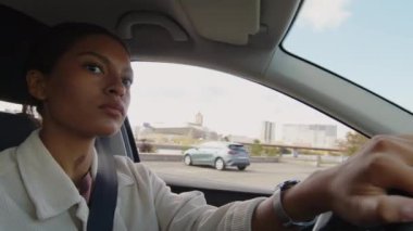 Yirmili yaşlarda çift ırklı bir kadının emniyet kemeri takılı solak bir araç kullanırken yakın plan fotoğrafı.