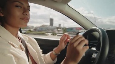 Mutlu, çift ırklı genç bir kadının, arabanın içinde oturmuş, kameraya bakıp, ehliyet sınavını geçtikten sonra neşeli bir şekilde gülümsemesi.