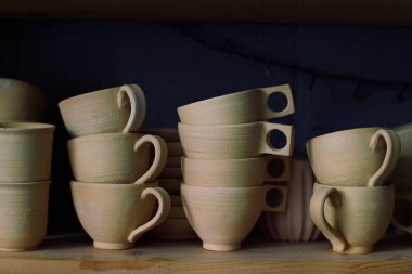 Çömlekçilik atölyesinde raftaki seramik bardakları kimse yakından çekmez.