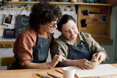 Down sendromlu bir öğrenciye çömlekçilik dersinde seramik kase yapmayı öğretirken orta boy beyaz kadın fotoğrafı.