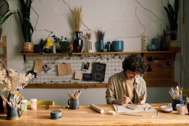 Neşeli kadın esnaf çömlek atölyesinde ahşap masada oturuyor yaprak şeklinde tabaklar yapıyor, boşluğu kopyalıyor.