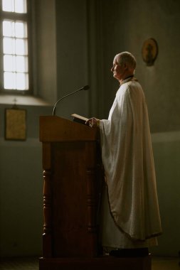 Yüksek katolik rahibin elinde mikrofonla kürsüde durup, uzayı kopyaladığı dikey yan görüntü.