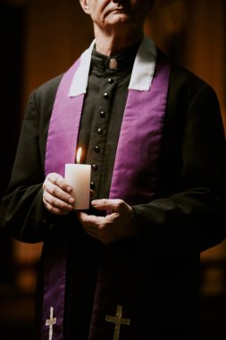 Kıdemli Katolik rahibin sutan giydiği ve ellerinde mum tuttuğu dikey ekin görüntüsü.