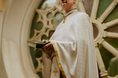 Kilisenin balkonunda elinde İncil kitabı tutan kıdemli Katolik rahibin düşük açılı görüntüsü.