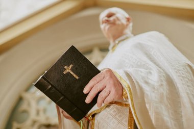 Kıdemli Kafkasyalı Katolik rahibin kırışık elleriyle dışarıda durup dini metinleri okuduğu düşük açılı bakış açısı.