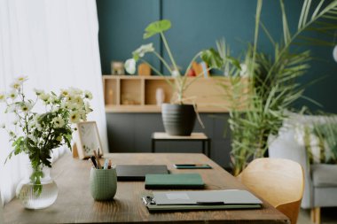 Ofis aksesuarları ve çiçek vazosuyla birlikte koyu yeşil ofisteki ahşap bilgisayar masasını kapat.