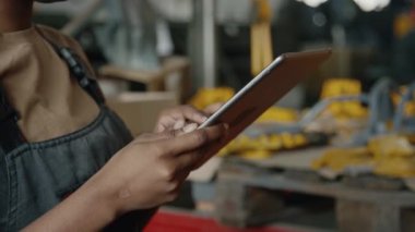 Genç siyahi kadın teknisyenin iş kıyafetlerinde endüstriyel fabrikayı teftiş ederken ve dijital tablet kullanırken yakın plan çekimleri.