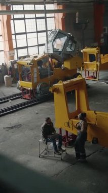 Erkek ve kadın teknisyenlerin traktör fabrikasında birlikte çalışırken tartıştıkları ve dizüstü bilgisayar ve tablet kullandıkları dik açılı bir çekim.