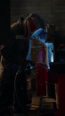 Korumacı yüz maskesi takan erkek endüstriyel işçinin dikey görüntüsü. Metal parçaları bitkiye kaynak yapıyor.