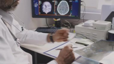 Beyaz önlüklü, erkek, çok ırklı x-ray doktorun, radyolojik hasta ayaklarının görüntülerini inceleyip anormallikleri saptadığı orta eğik bir çekim.
